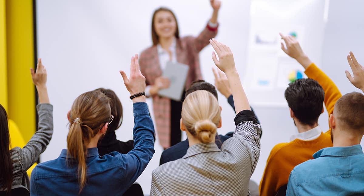 Group of young people sitting at a conference together raised ha